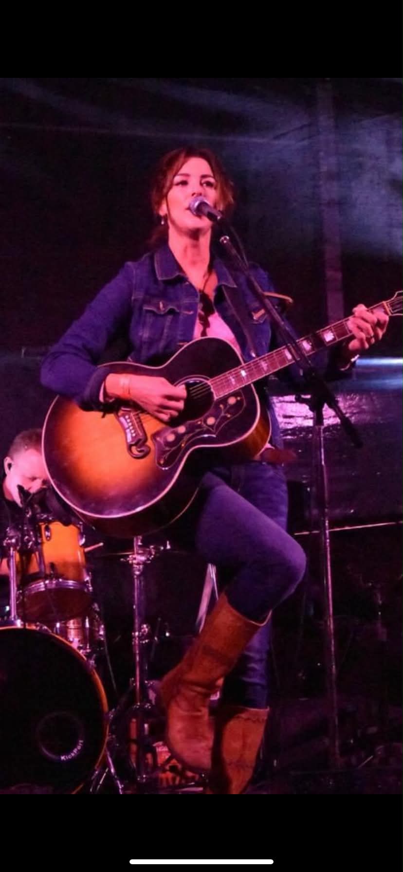 Karla Crawford performing on stage with acoustic guitar